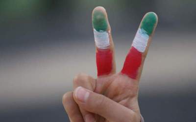 شرح عکس: دو انگشت که به نشانه پیروزی (V) نگاه داشته شده‌اند و با رنگ‌های پرچم ایران رنگ‌ آمیزی شده‌اند در راهپمایی ۲۲ بهمن ۱۴۰۲ قم
